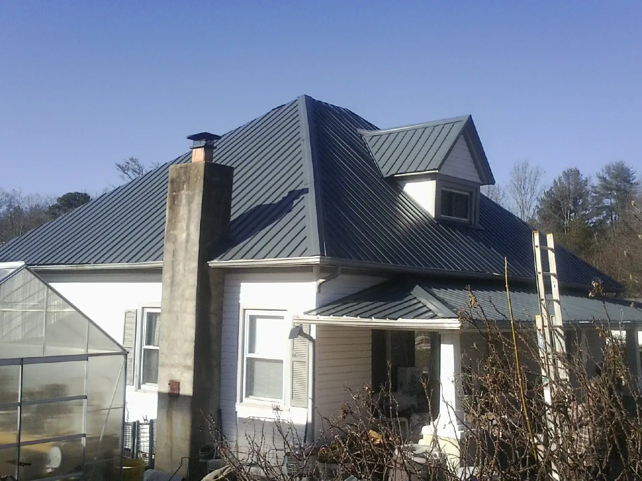 Dark blue standing seam metal roof on a white farmhouse with dormer — Slate & Tile Roof Repair by Roofing Brothers in Northfork
