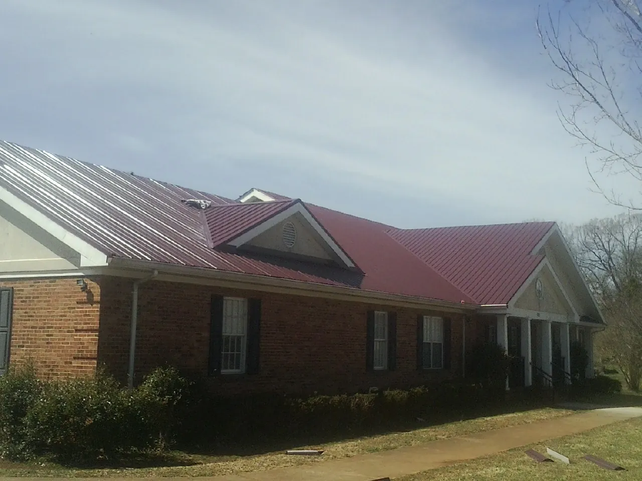 Red metal roof with gabled entries on a long brick building, from a Hail Damage Roof Repair job in Northfork