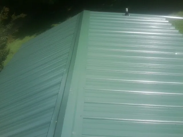 New green metal panels meeting at the ridge of a roof — Flat Roof Repair work by our crew in Northfork