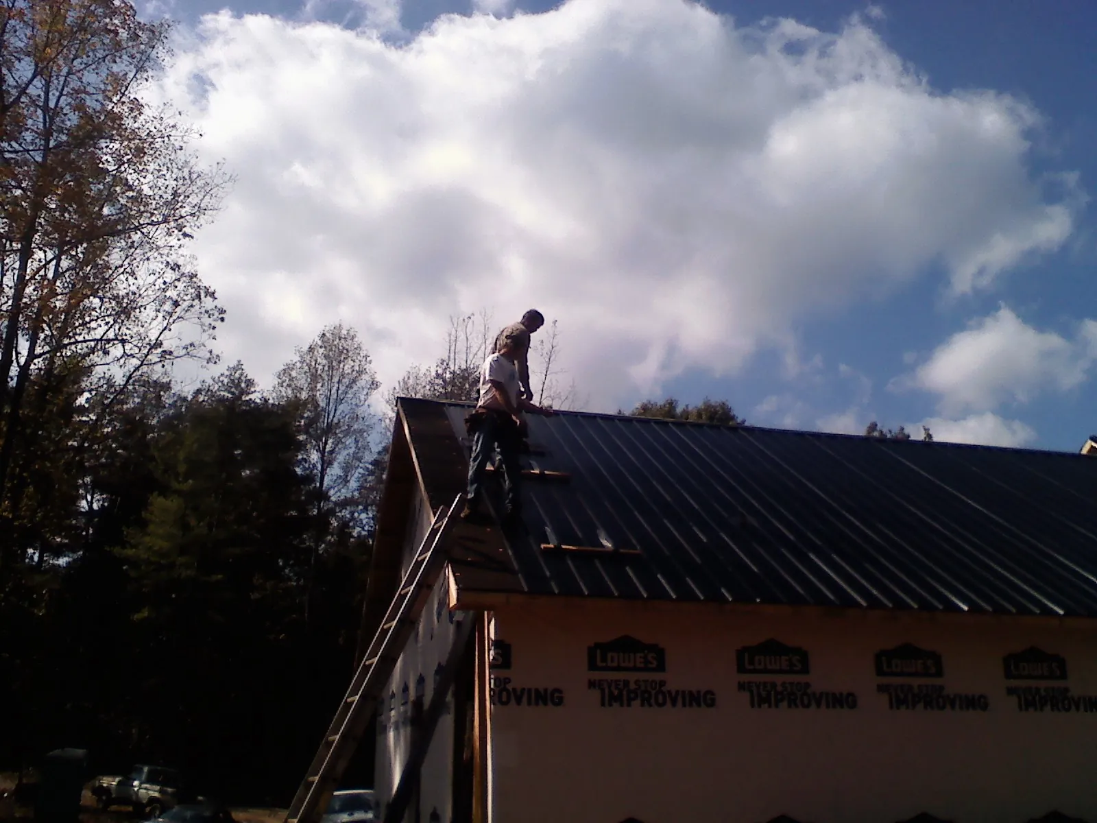Roofer fastening dark metal panels high against a cloudy sky, from a Roof Inspection job in Northfork