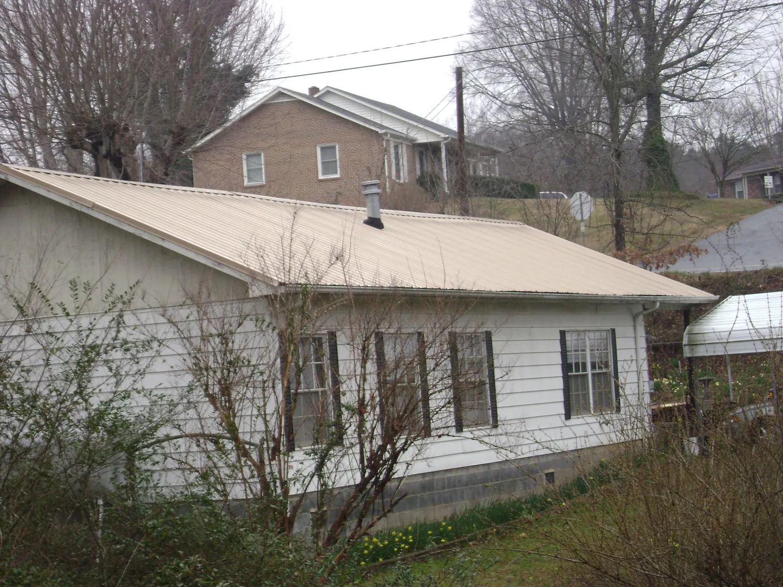 Tan metal roof on a white sided house set into a hillside — Commercial Roofing by Roofing Brothers in Northfork